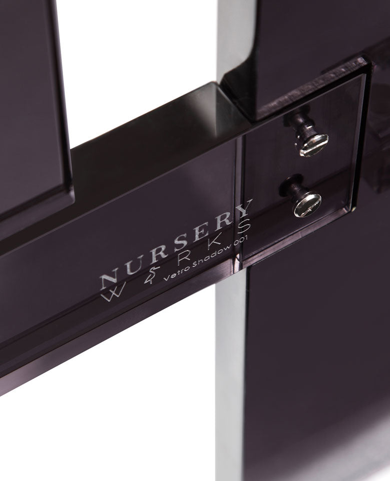 Close-up of a black object with the engraved text "Nursery Works Vetro Shadow 001" and two visible screws.